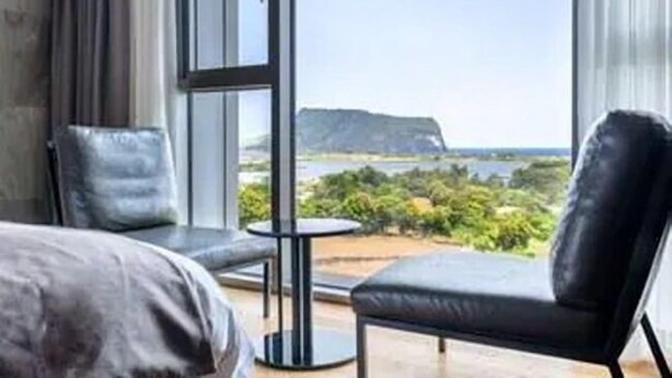 Et moderne hotelværelse med et stort vindue, der giver udsigt til et bjerglandskab og et vandområde.