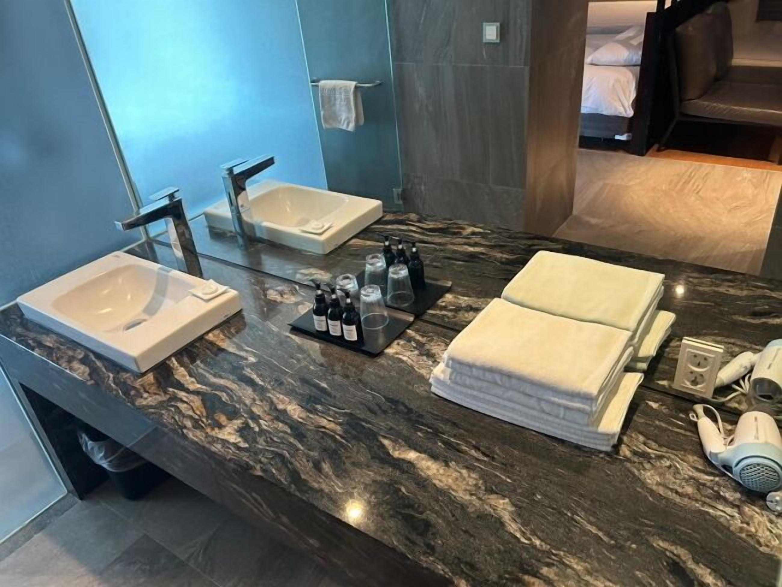 A modern bathroom with a marble countertop, two sinks, a towel rack, and a hairdryer.