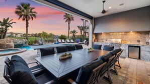 An outdoor dining area with a pool, palm trees, and a modern kitchen. - The Luxe Palmilla | Private Pool and Spa, Custom-Themed Kids Bedrooms (Kissimmee)