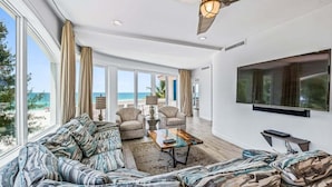 A spacious living room with a large sofa, two armchairs, a coffee table, and a flat-screen TV mounted on the wall. - Anna Maria Grand: Gulf Front! On the Beach! Sleeps 22 by Anna Maria Life Vacation Rentals (Bradenton Beach)