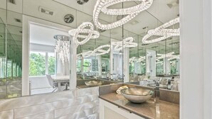 A modern bathroom with a large mirror, a bowl on the counter, and a chandelier. - Anna Maria Grand: Gulf Front! On the Beach! Sleeps 22 by Anna Maria Life Vacation Rentals (Bradenton Beach)