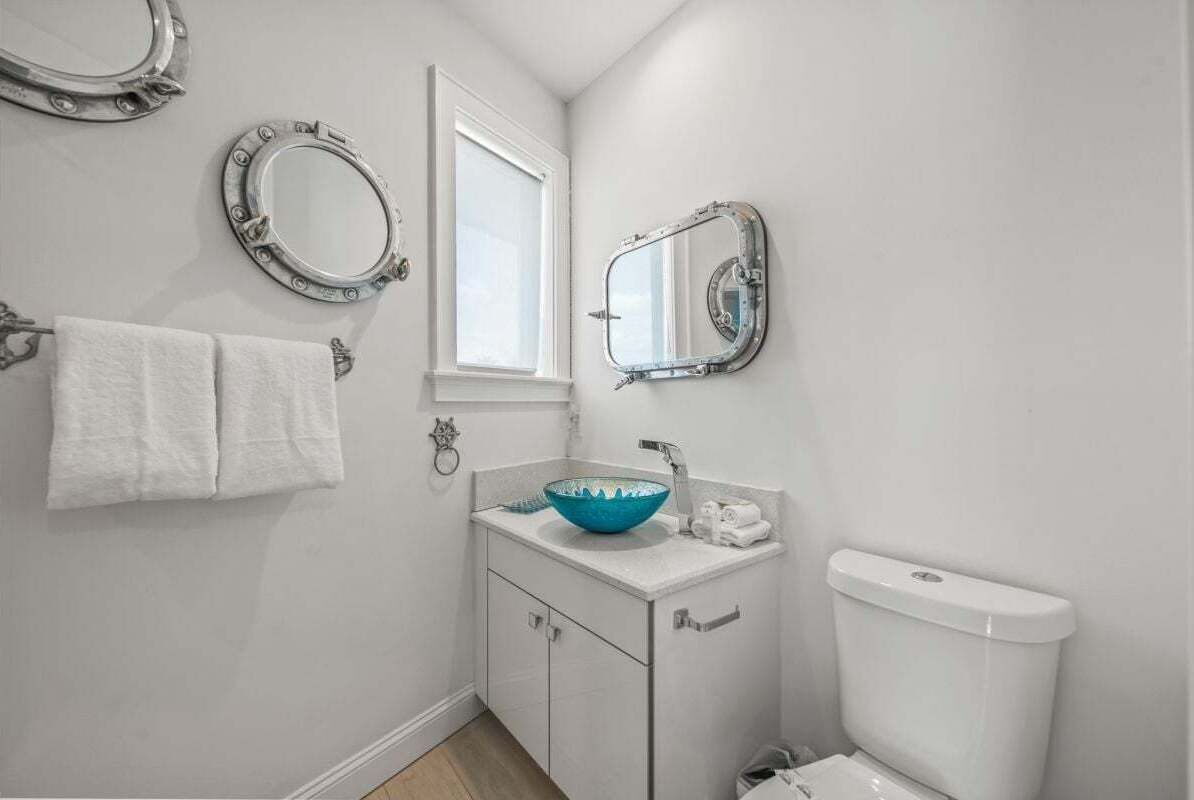 A small bathroom with a white sink, a blue bowl, a white toilet, and two mirrors.