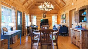 A wooden cabin interior with a dining table, chairs, a television, and a fireplace. - Annie's Cabin | Pet Friendly | Mountain View | Hot Tub | Fire Pit (Fairview)