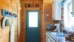 A cabin interior with a blue door, wooden walls, a kitchen area with a sink and fruit bowl, and decorative plates on the wall. - Annie's Cabin | Pet Friendly | Mountain View | Hot Tub | Fire Pit (Fairview)