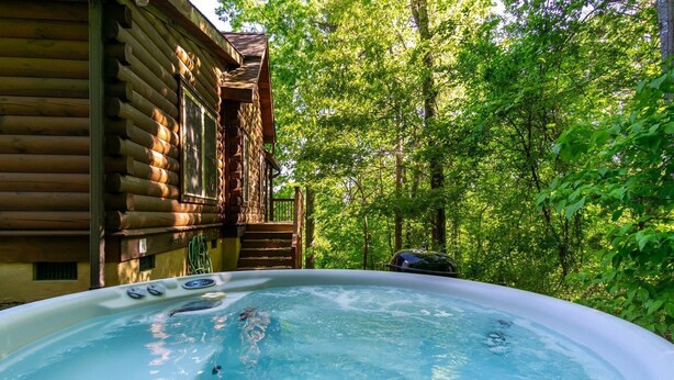 A hot tub in a forested area with a wooden cabin in the background. - Annie's Cabin | Pet Friendly | Mountain View | Hot Tub | Fire Pit (Fairview)