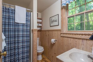 Un baño con tocador de madera, lavamanos blanco, inodoro y cortina de ducha.