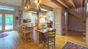Ein rustikales Blockhaus-Interieur mit einem Holzessttisch, Stühlen, einer Küchenzeile und einer Treppe.