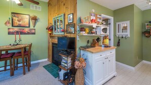 A cozy room with a wooden ceiling fan, a fireplace, a dining area with a table and chairs, and a kitchen area with a microwave and cabinets.