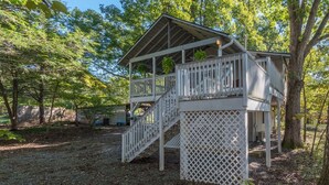 A wooden deck structure with a staircase leading to a covered area, surrounded by trees.