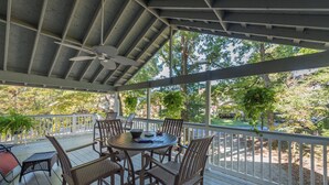 A covered outdoor patio with a round table and chairs, surrounded by a white railing.