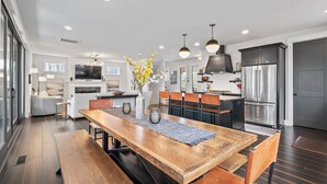A modern kitchen with a wooden dining table, built-in appliances, and pendant lighting. - Birdsong | Fire Pit & Easy Access to Lake James! (Nebo)
