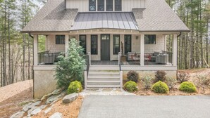 A two-story house with a covered porch, stone steps, and a small tree in the front yard. - Birdsong | Fire Pit & Easy Access to Lake James! (Nebo)