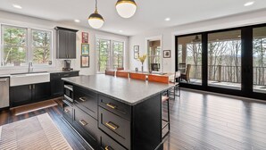 A modern kitchen with dark cabinetry, a large island, and pendant lighting. - Birdsong | Fire Pit & Easy Access to Lake James! (Nebo)