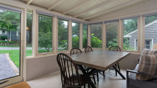 A conservatory with a large table and chairs, large windows, and a view of a garden and houses. - Little Piney | Pet Friendly & Golf Course Views! (Black Mountain)