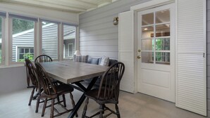 A dining area with a wooden table and chairs, a bench with cushions, and a white door with glass panels. - Little Piney | Pet Friendly & Golf Course Views! (Black Mountain)
