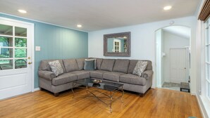 A living room with a sectional sofa, a glass coffee table, and hardwood flooring. - Little Piney | Pet Friendly & Golf Course Views! (Black Mountain)
