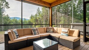 Un espacio de estar al aire libre cubierto con un sofá modular y una mesa de centro de vidrio, con vistas a un paisaje boscoso.