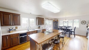 A spacious kitchen with wooden cabinets, a central island with bar stools, a dining area with a chandelier, and large windows providing natural light. - Delightful 6 bedroom house on Paradise Valley Country club golf course (Casper)