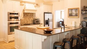 Una cucina moderna con mobili bianchi, una grande isola con sgabelli da bar, elettrodomestici in acciaio inossidabile e una parete rivestita di piastrelle.