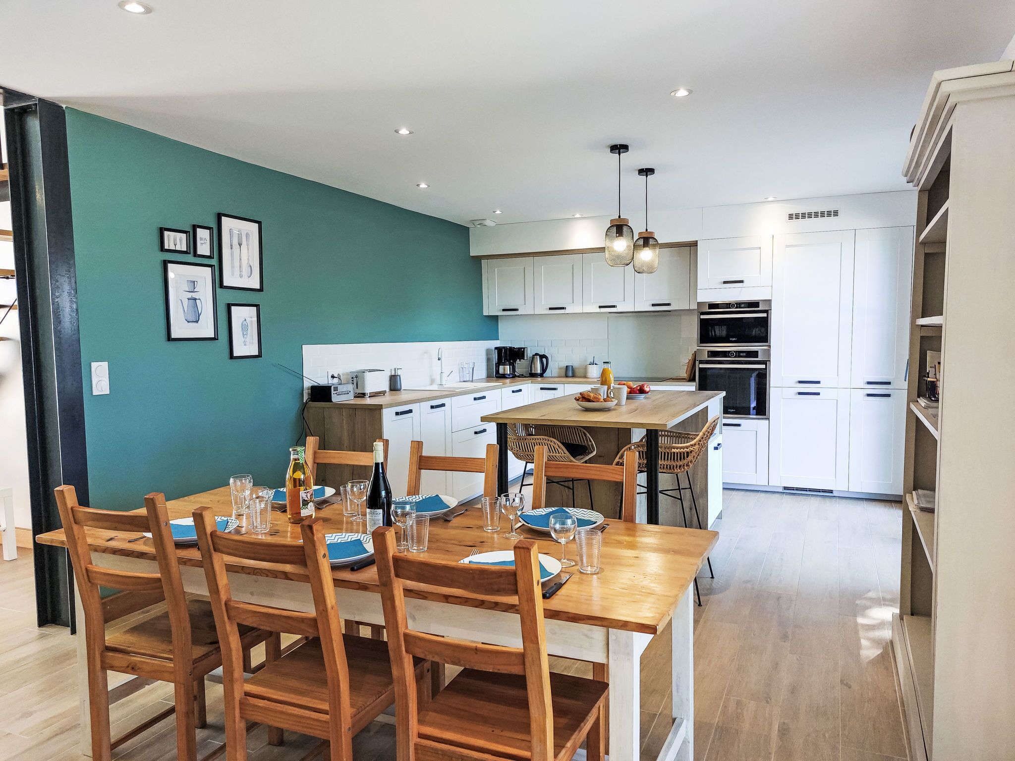 A modern kitchen with white cabinets, a wooden dining table, and a teal accent wall.