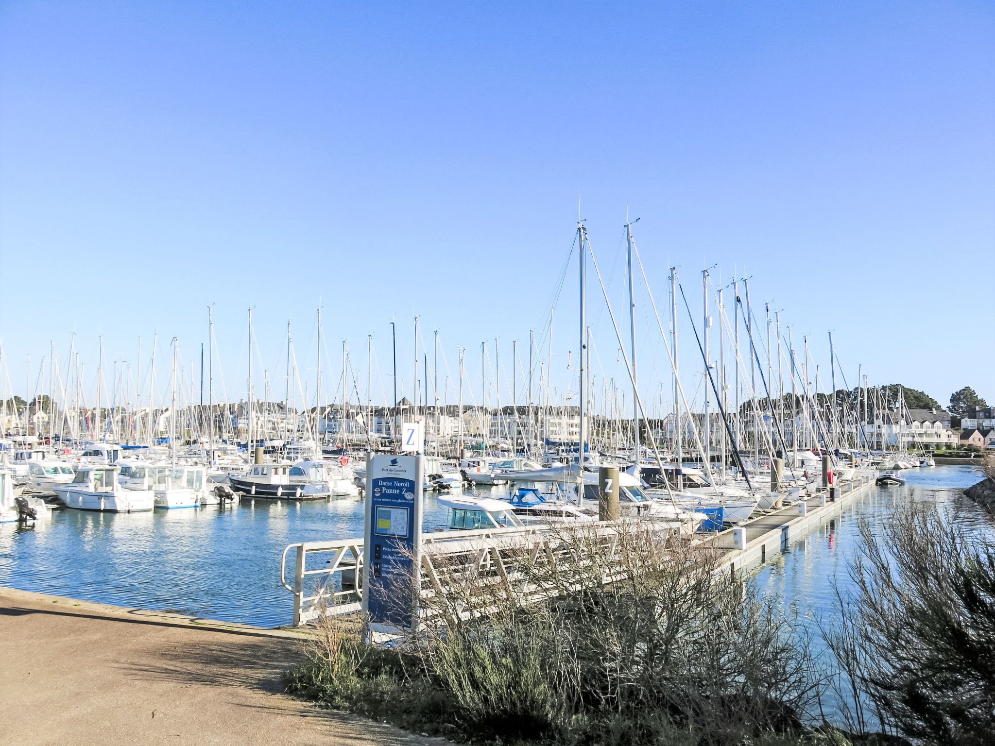 Ein Yachthafen mit zahlreichen vor Anker liegenden Booten, einem klaren Himmel und einem Schild mit der Aufschrift 'Port de Granit'.