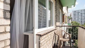 Un balcón con pared de ladrillo, una ventana con cortina y una silla de plástico, además de un toldo verde.