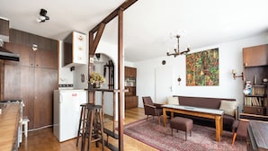Cocina compacta con refrigerador, taburetes de bar y zona de comedor con sofá y mesa.