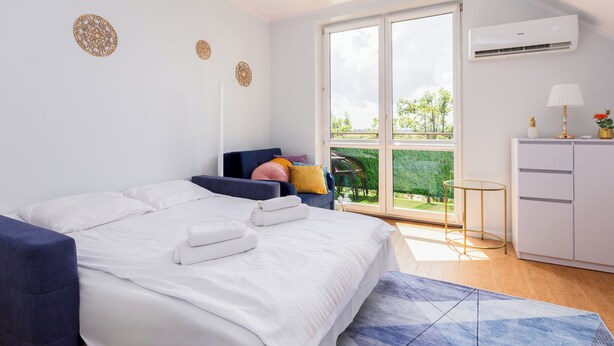 Un dormitorio moderno con una cama grande, un sofá, una mesita y vista a un jardín por una puerta corredera.
