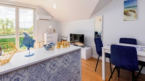 Una sala moderna con un ventanal grande, una chimenea, un televisor y una zona de comedor con una silla azul.