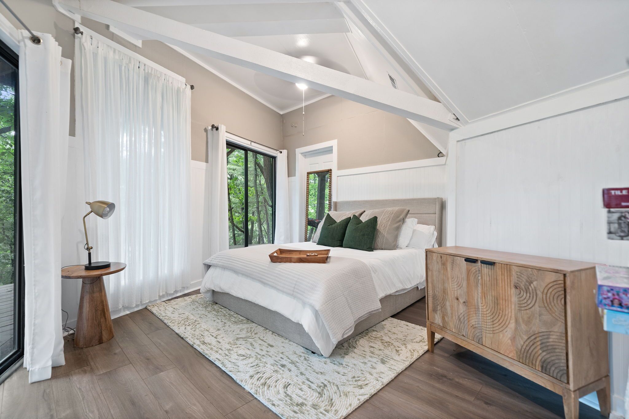 A bedroom with a bed, a bedside table, a wooden cabinet, and a large window with curtains.