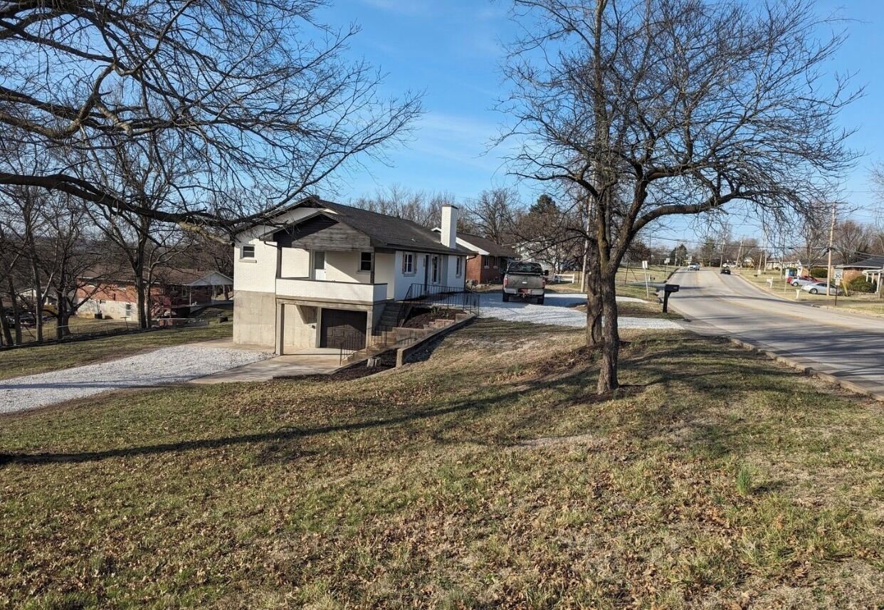 A residential street with houses, a driveway, and a parked vehicle.