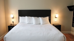 A neatly made bed with white linens and a dark headboard, flanked by two bedside tables with lamps. - The Principal Hotel (Columbia)