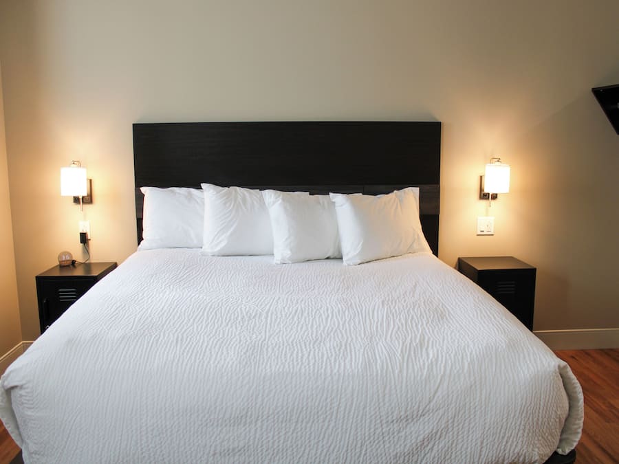 A neatly made bed with white linens and a dark headboard, flanked by two bedside tables with lamps.