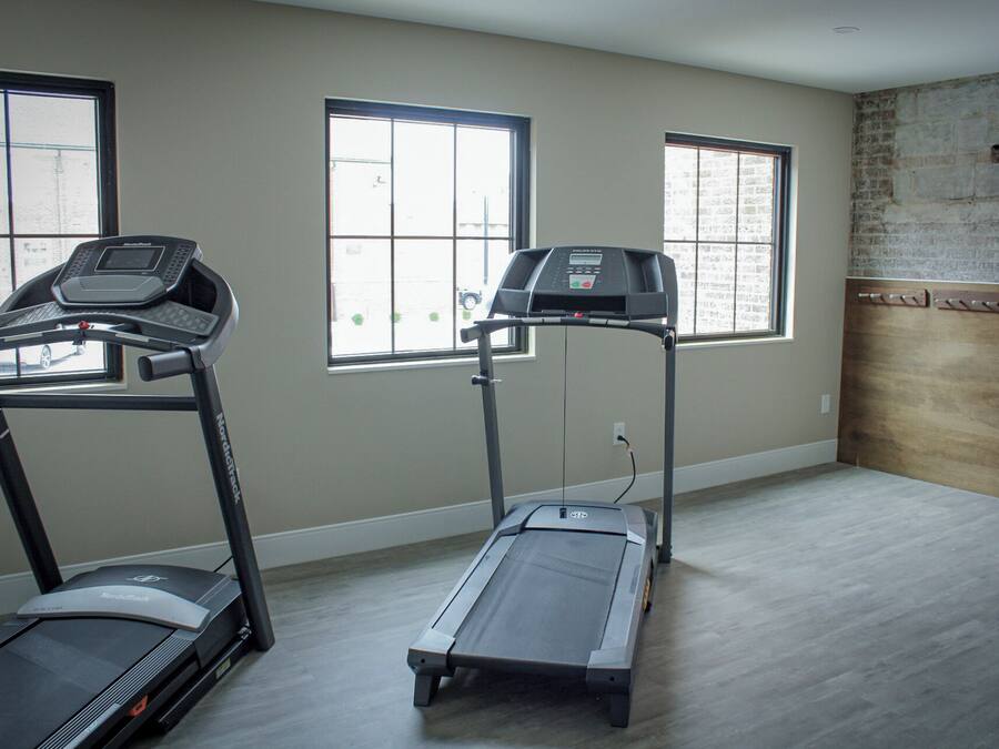 A room with two treadmills, large windows, and a brick wall.