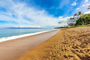 Une plage avec un ciel dégagé, des vagues sur l’océan et des empreintes de pas dans le sable.
