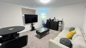 A living room with a flat-screen TV, a coffee table, a sofa with cushions, a dining table, and a refrigerator. - Entire Guest Suite/Separate Entrance/Free Parking in Winnipeg (Winnipeg)