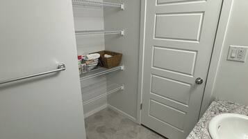 A bathroom with a white door, a sink with a marble countertop, and shelves with baskets and toiletries.