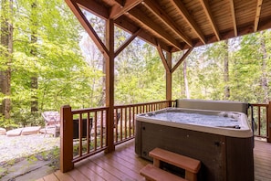 A wooden deck with a hot tub, wooden benches, and a view of a forest.