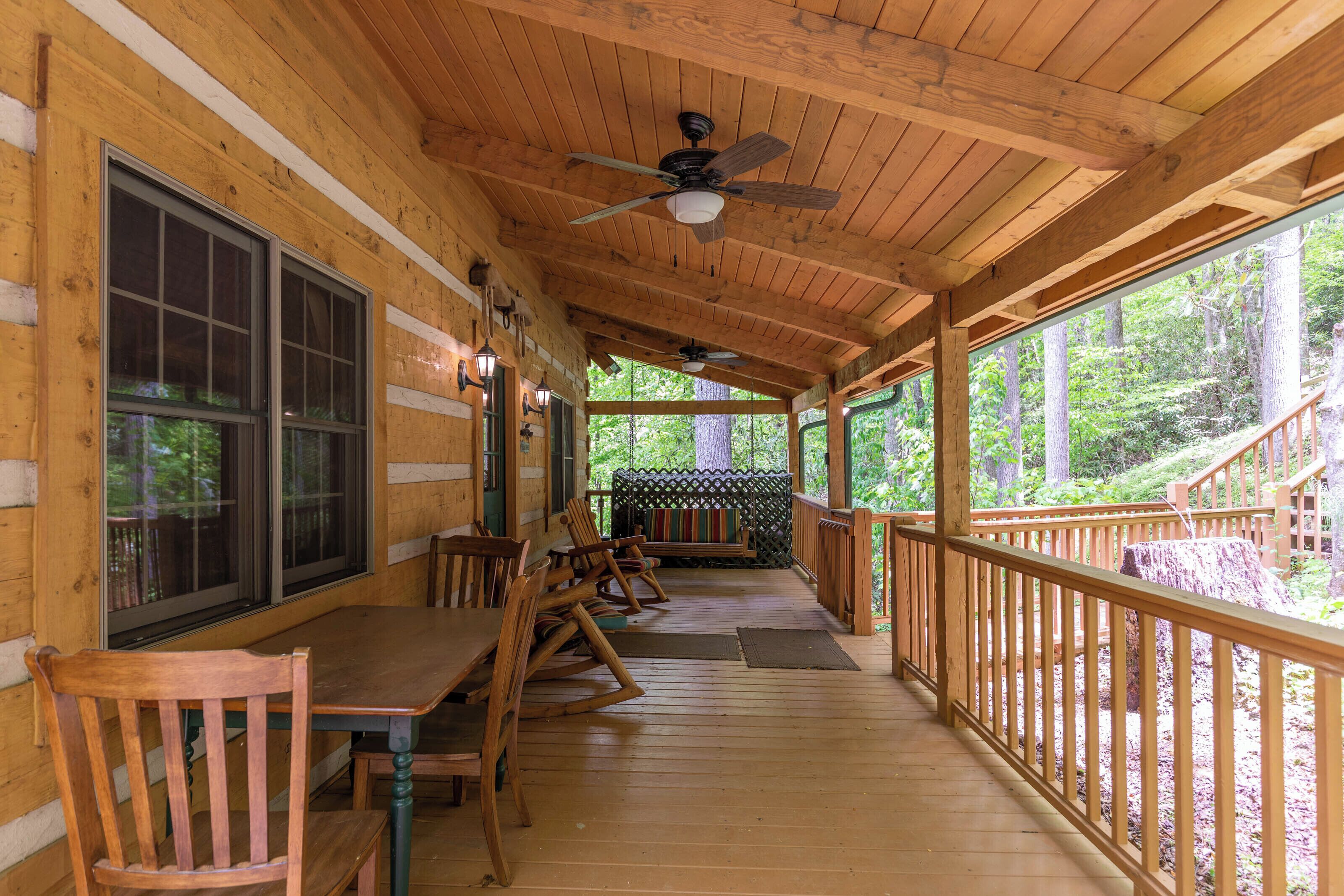 A wooden deck with a covered seating area, wooden chairs, and a table.