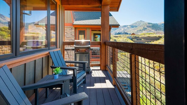 Una terraza de madera con mobiliario exterior, una parrilla y vistas a un paisaje montañoso.