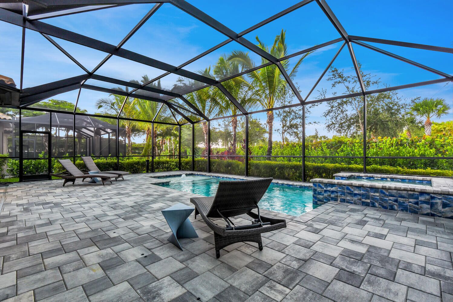 A covered outdoor swimming pool area with lounge chairs and a view of palm trees.