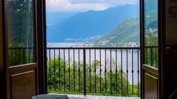 Quarto com varanda com vista para um lago e montanhas.