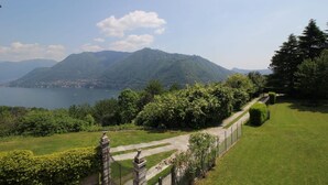 Um jardim bem cuidado com um caminho, um muro de pedra e vista para um lago e montanhas.