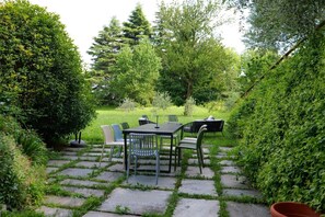 Un patio con mesa y sillas, rodeado de follaje y árboles.