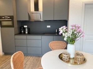 A modern kitchen with grey cabinets, a stainless steel range hood, a coffee maker, and a vase with flowers on a table.