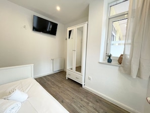 Une chambre à coucher comprenant un lit, une armoire, un téléviseur, un radiateur et une fenêtre avec des rideaux.