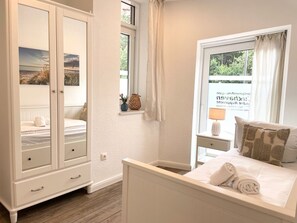 Un dormitorio con cama, armario, ventana con cortinas y vistas al exterior.