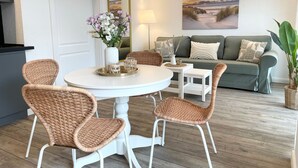 A living room with a round table, wicker chairs, a sofa, a painting, and a potted plant. - NB 3 - Stylish vacation apartment with private sauna and whirlpool bath - House (Cuxhaven)