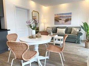 Un salon avec une table ronde, des chaises en osier, un canapé, un tableau et une plante en pot.