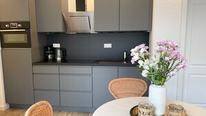 Una cocina moderna con gabinetes grises, una campana extractora de acero inoxidable, una cafetera y un florero con flores sobre una mesa.